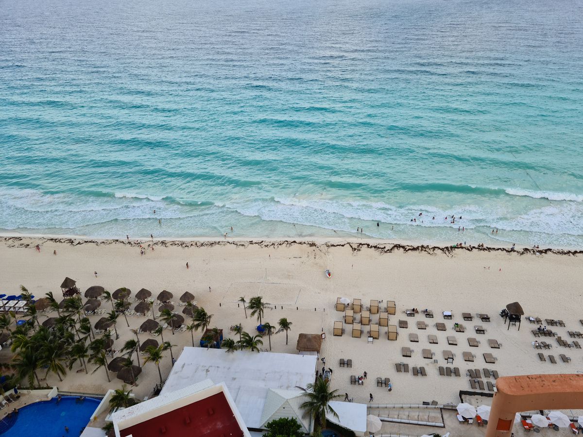 Vista aérea de una playa de resort con personas disfrutando el verano junto a la orilla del mar.