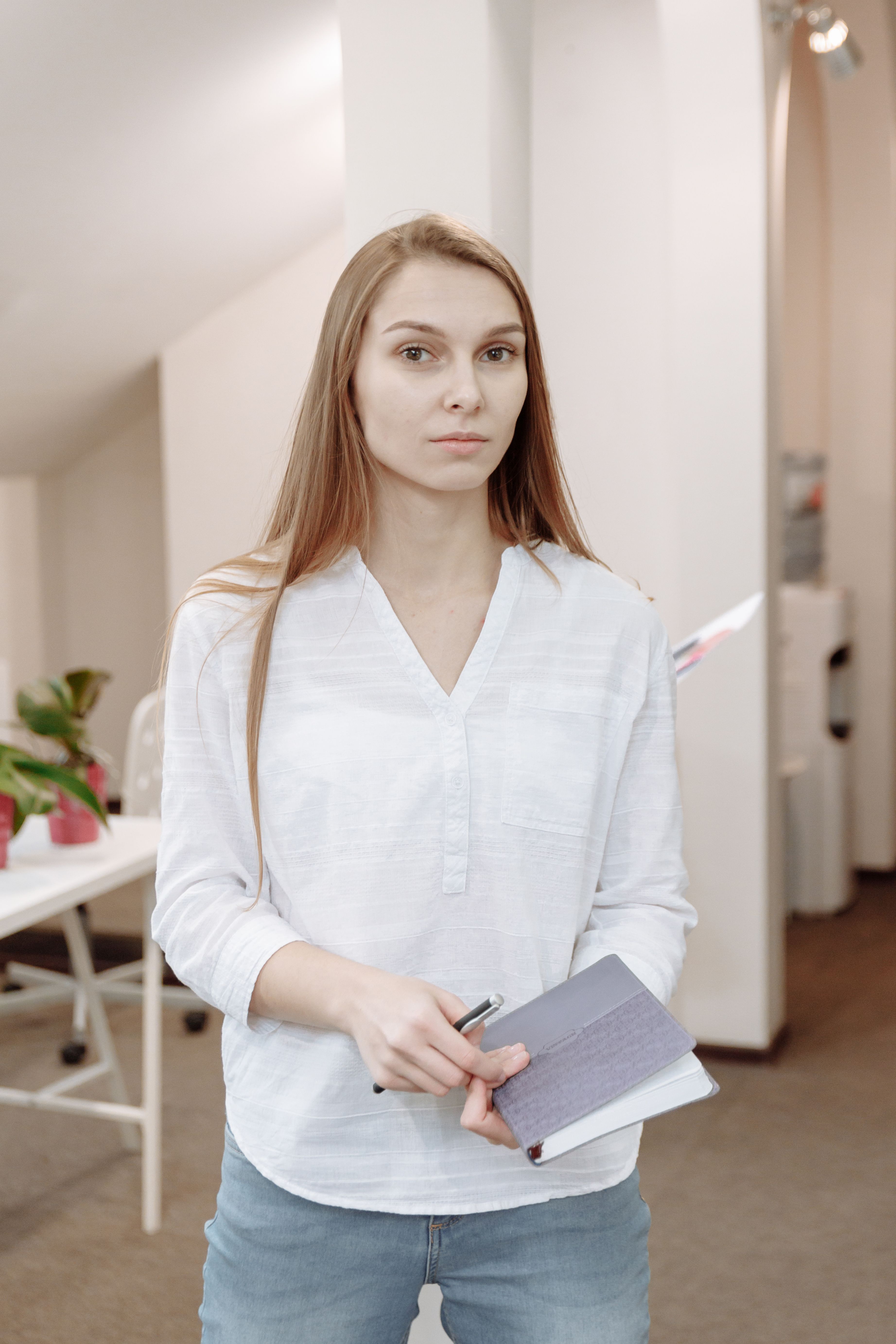 一位穿着办公室服装的白人妇女拿着笔记本和笔，站在现代工作场所里