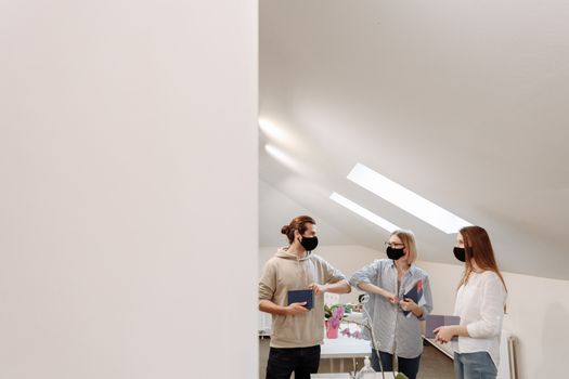 Three colleagues discuss in an office setting while wearing face masks, maintaining COVID-19 protocols.