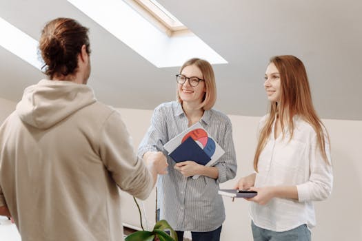 Three coworkers in an office meeting, shaking hands and discussing ideas.
