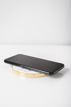 A sleek black smartphone placed on a wireless charger with a modern white background.