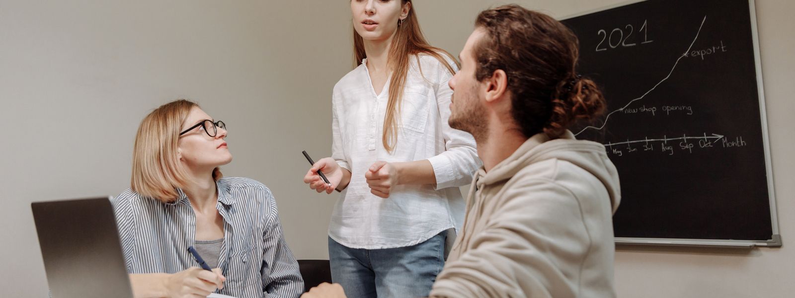 Co-workers engaged in a group discussion around a desk in an office environment.
