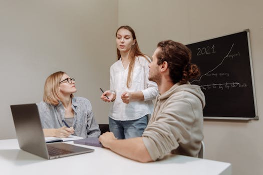 Co-workers engaged in a group discussion around a desk in an office environment.