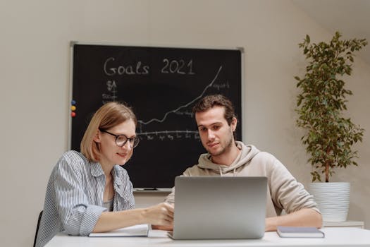 Two coworkers collaborating on 2021 goals in a modern office setting with a laptop.