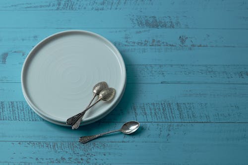 White Ceramic Plates With Teaspoons On Blue Wooden Surface