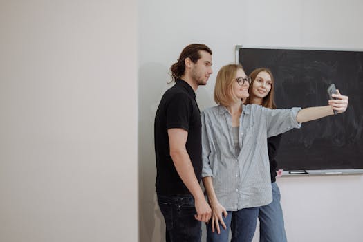 Three young adults taking a selfie in a casual office setting, displaying teamwork and camaraderie.
