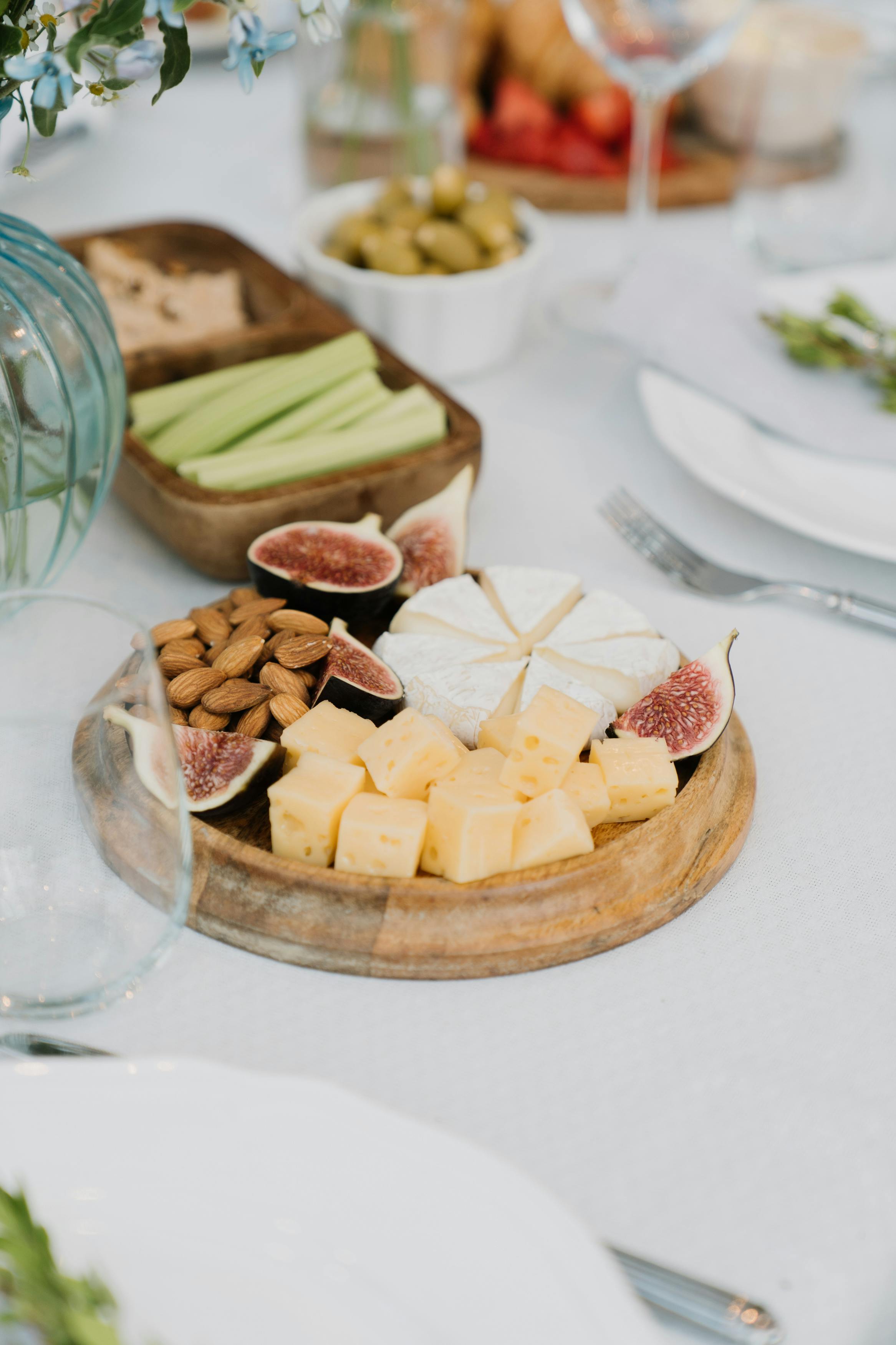 Gourmet cheese platter with figs, almonds, and celery sticks on a wooden tray. Perfect for party appetizers.