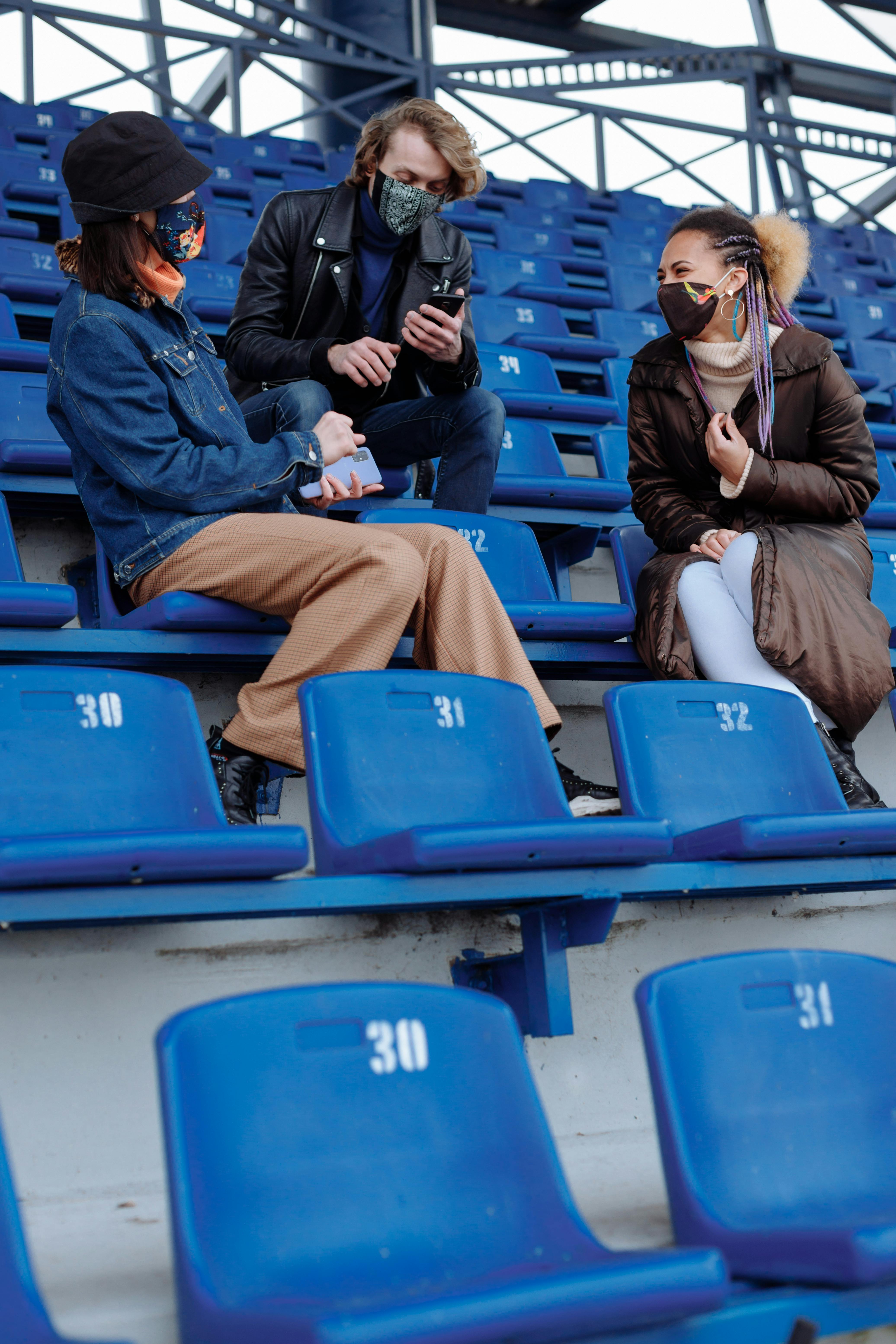 people in jackets and face masks sitting on blue chairs