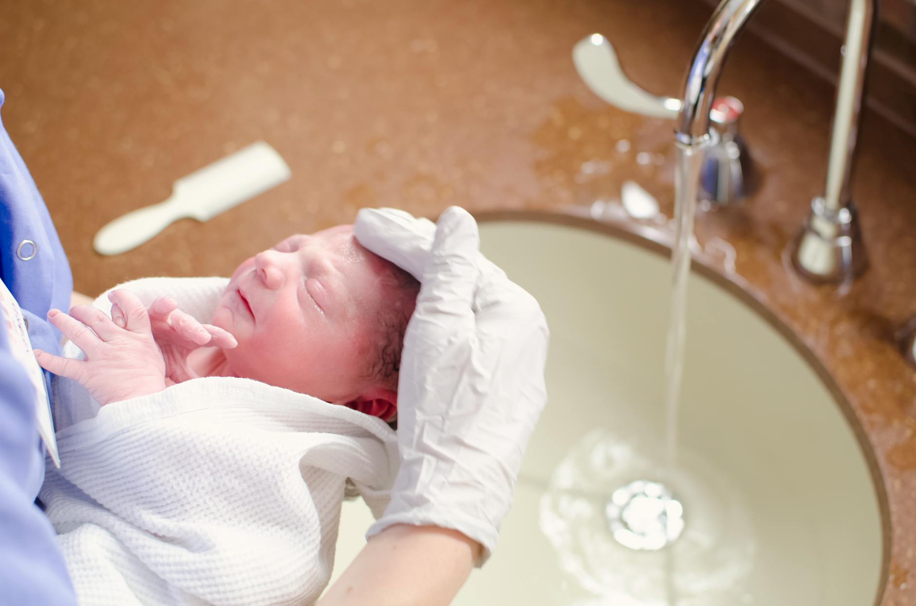 A nurse gently bathes a newborn in a hospital sink, ensuring care and hygiene.