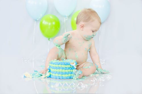 Free Adorable baby enjoying a messy cake smash during a colorful birthday celebration. Stock Photo