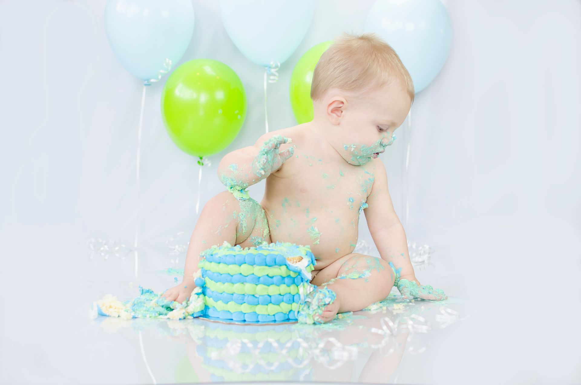 Adorable baby enjoying a messy cake smash during a colorful birthday celebration.