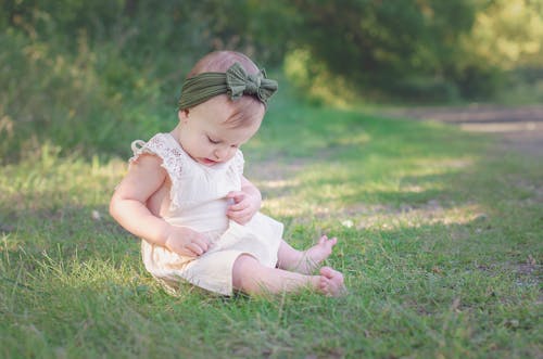 Cute Toddler in a White Dress Sitting on the Grass