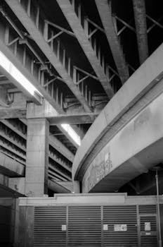 Black and white of heavy industrial construction with tall massive columns illuminated with bright light