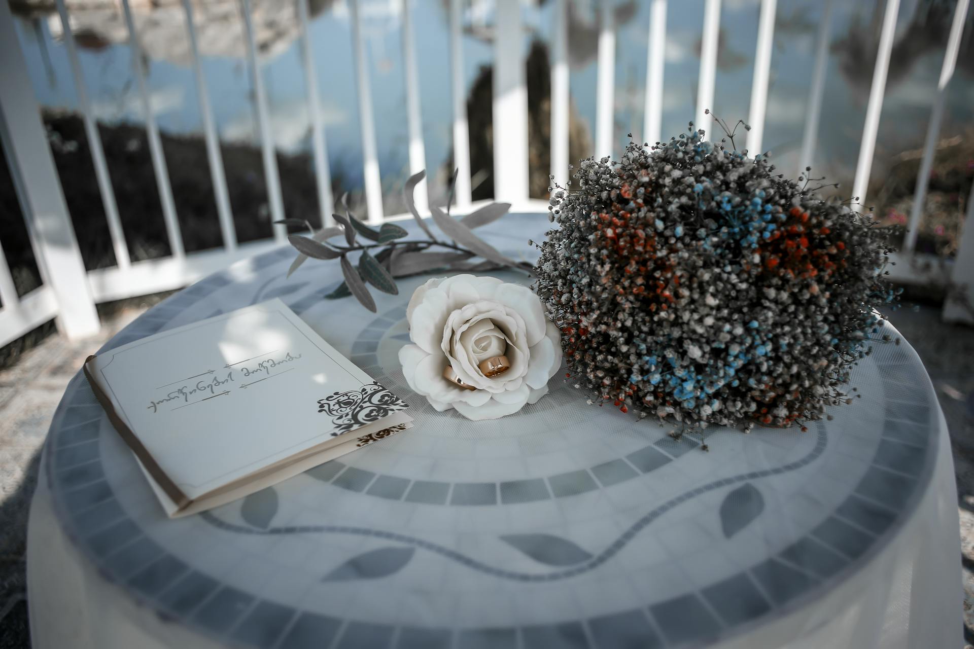 A charming floral bouquet, rose, and wedding invitation on an outdoor table.