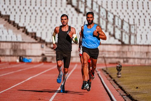 Free Two male runners competing on a stadium track during a sunny day. Stock Photo