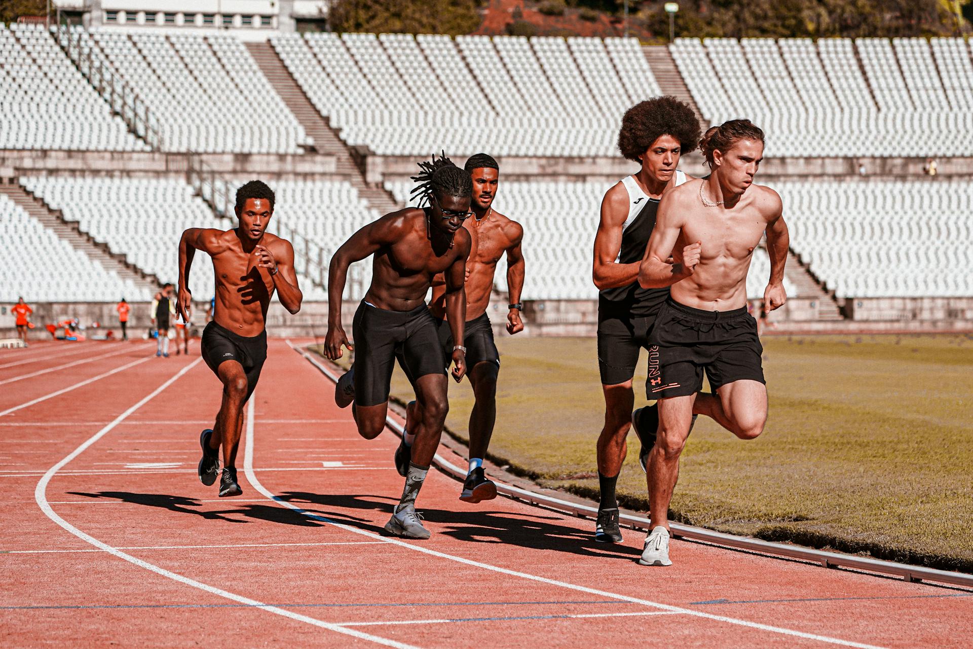 Five men sprinting on a stadium track, showcasing athleticism and competition.
