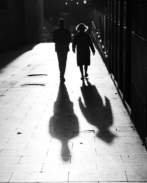 Grayscale Photo of Man and Woman Walking on Sidewalk