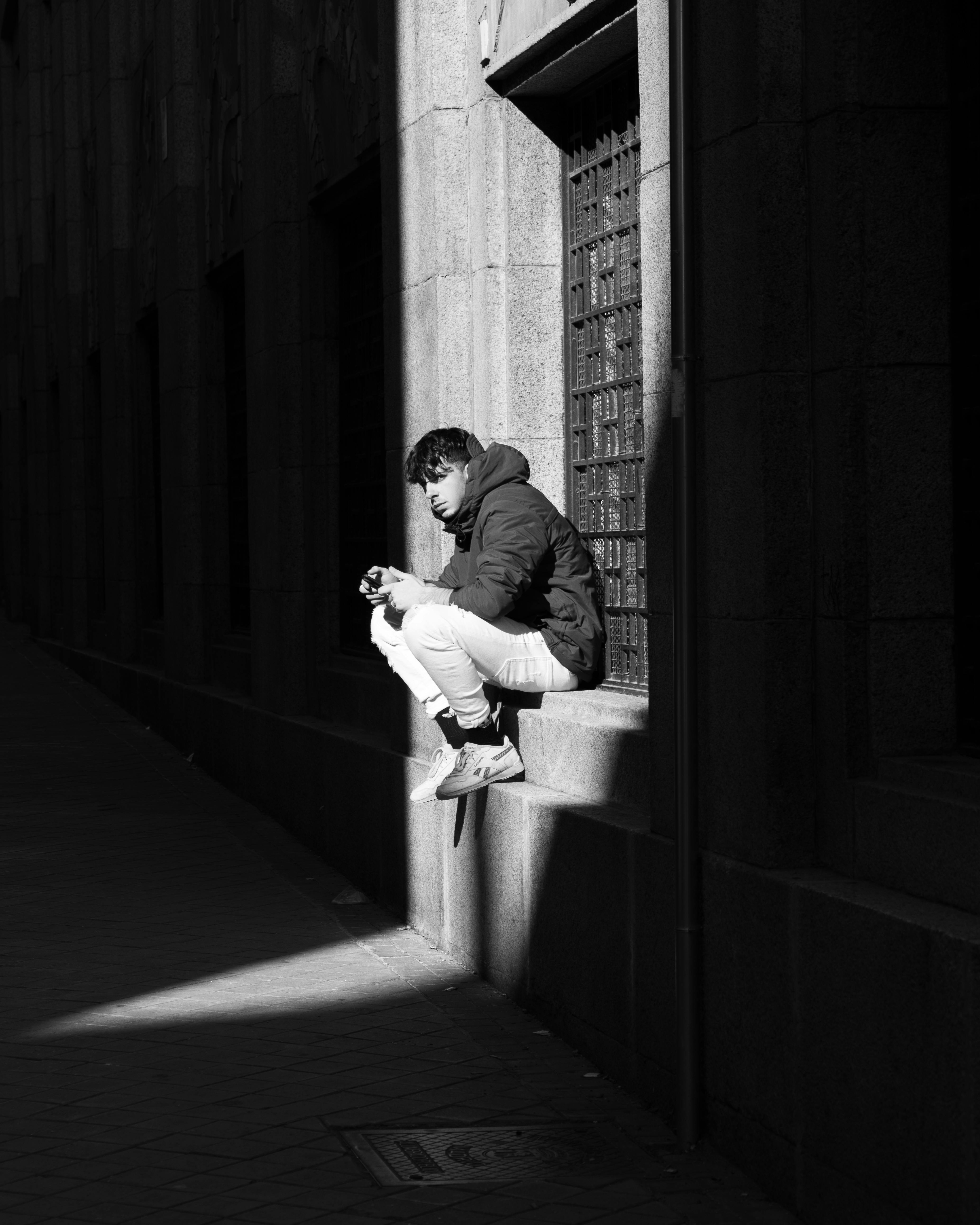 Monochrome image of a man sitting on a ledge, captured in Madrid, Spain.
