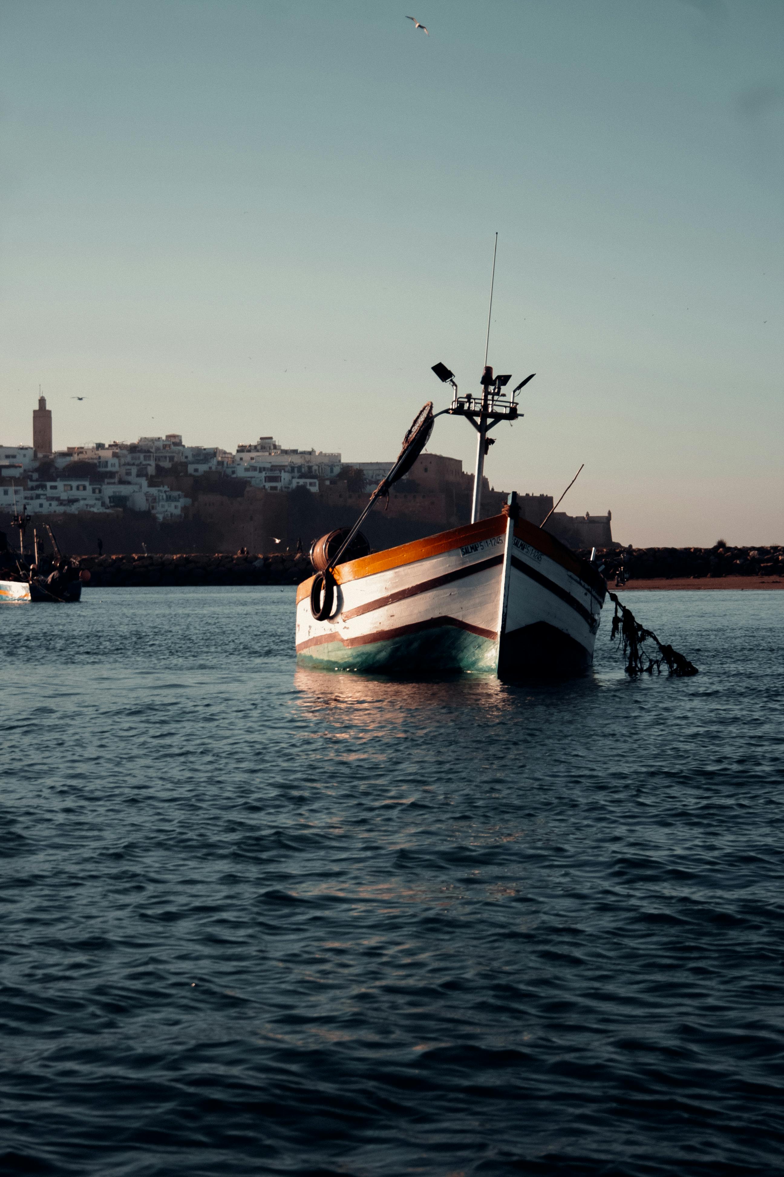 Free A scenic view of a traditional boat in Rabat harbor during sunset with a historic city backdrop. Stock Photo