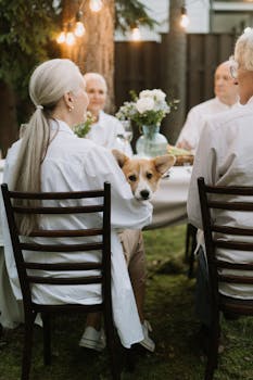 Elderly friends enjoy an outdoor dinner party with a corgi dog.