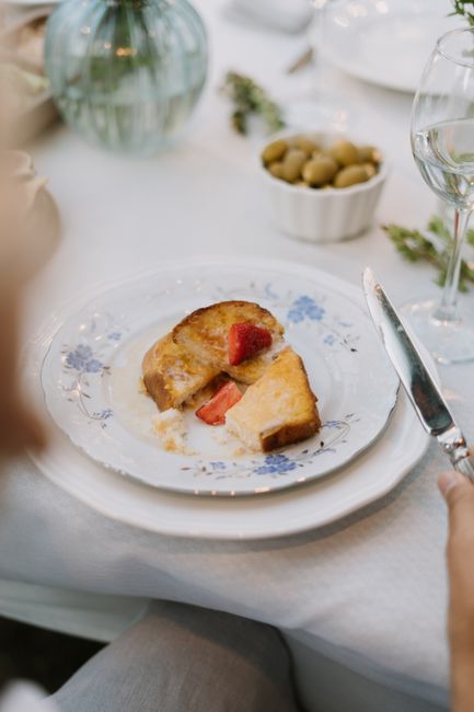 Two golden-brown stuffed french toast halves stacked on a plate, oozing sweet cream cheese filling and dusted with powdered sugar alongside fresh strawberries and maple syrup.