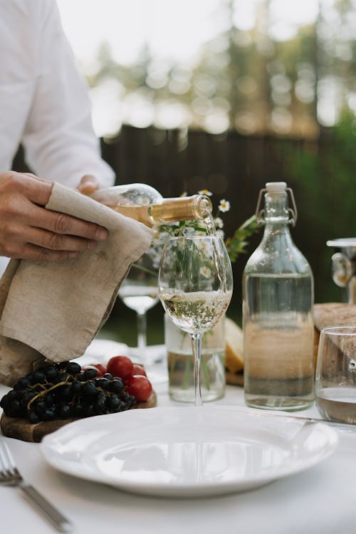 Person Pouring White Wine on a Clear Glass