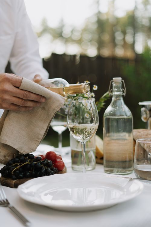 Free Hands pouring white wine into a glass at an elegant outdoor table with grapes and bread. Stock Photo