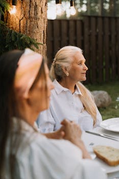 An elderly woman enjoying a peaceful outdoor dinner with family under cozy lighting.