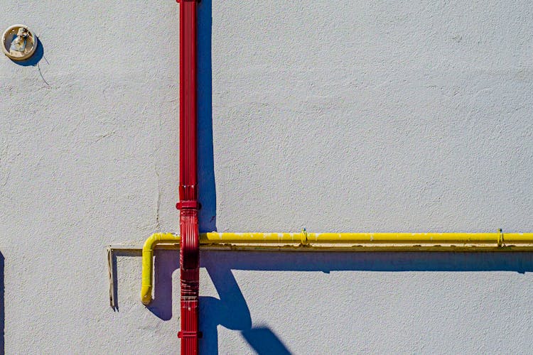 A Pipe And A Downspout On A White Concrete Wall