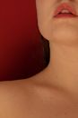 Unrecognizable enigmatic female with bare shoulders and wet hair standing on red background with drops on face in modern studio