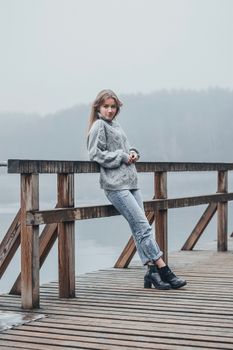 一位穿着毛衣的女人站在雾蒙蒙的木码头上，感受着秋天的气息