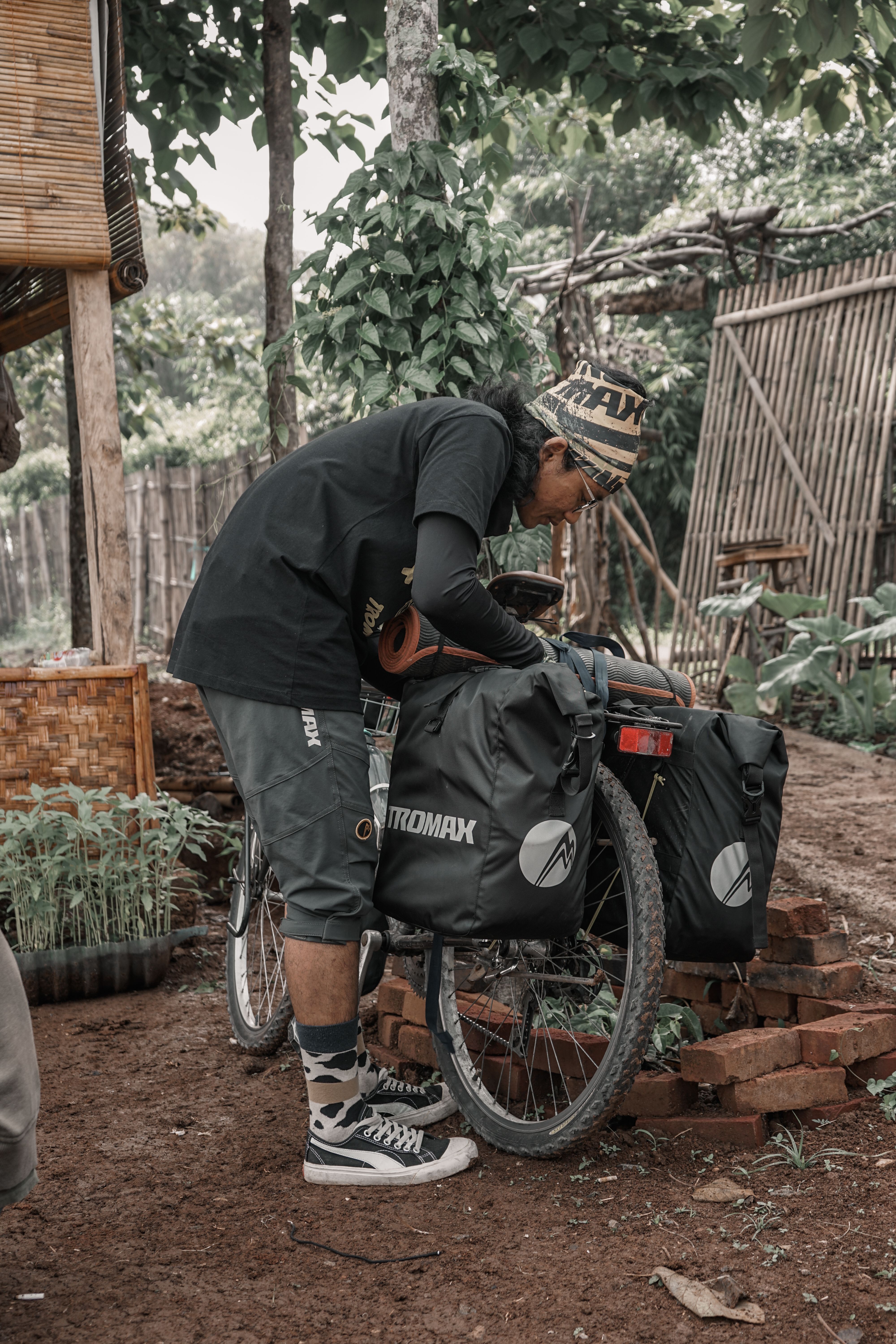 A cyclist inspects bags attached to a bicycle in an outdoor setting.