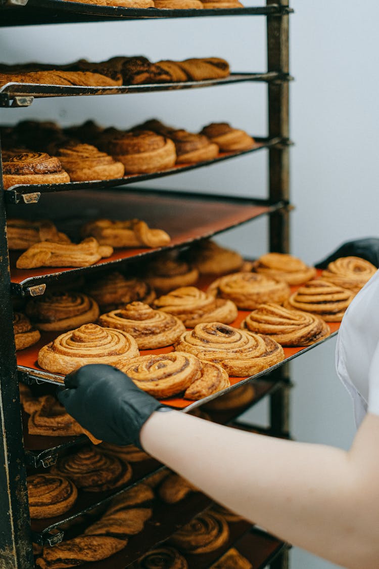 Person Putting Freshly Baked Cinnamon Rolls In A Food Rack