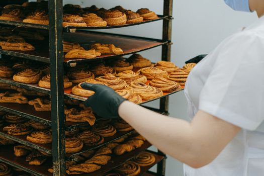 面包师把刚烤好的肉桂卷放在面包店厨房的冷却架上