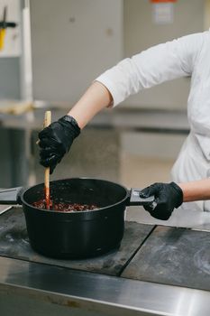 A chef stirs a dish in a black pot, highlighting culinary preparation in a professional kitchen.