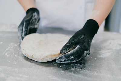 Gloved hands pressing out a round of pale dough on a steel bench