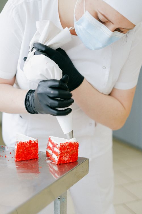 Free A pastry chef in uniform decorates red velvet cake slices with icing. Stock Photo