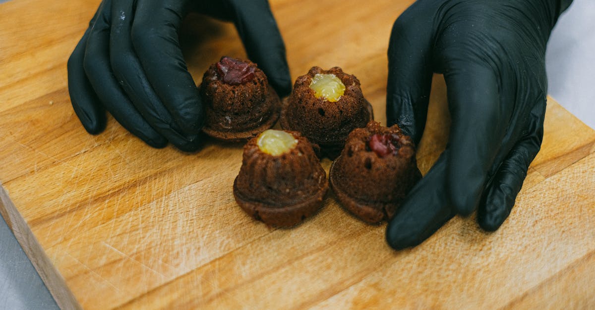 Close-up of gourmet mini cupcakes on a wooden board, handled by gloved hands.