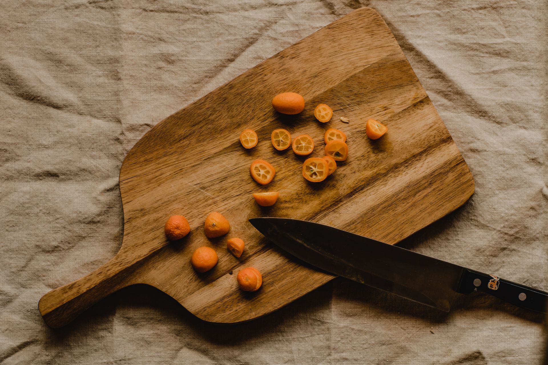 Fresh kumquats sliced on a wooden board with a knife, offering a rustic aesthetic from above.