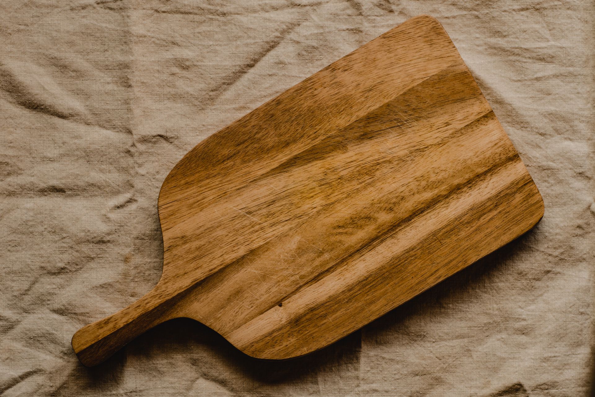 Rustic wooden chopping board on textured linen surface for kitchen decor