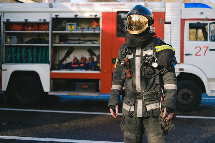 A Firefighter In Uniform Standing Near A Fire Truck