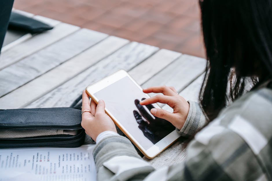 preparing for a due diligence process - A young woman using a tablet for studying outdoors at a wooden table.