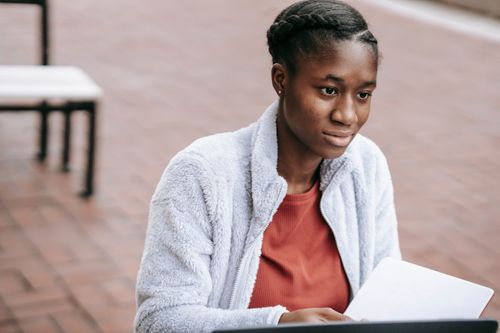 Free High angle of calm young African American female student with opened notepad sitting at table in campus while doing home task Stock Photo
