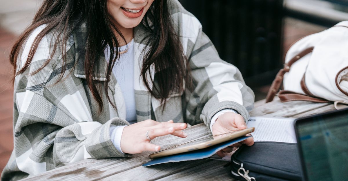 High angle of happy young Asian female student working on tablet while doing home task sitting at table in campus