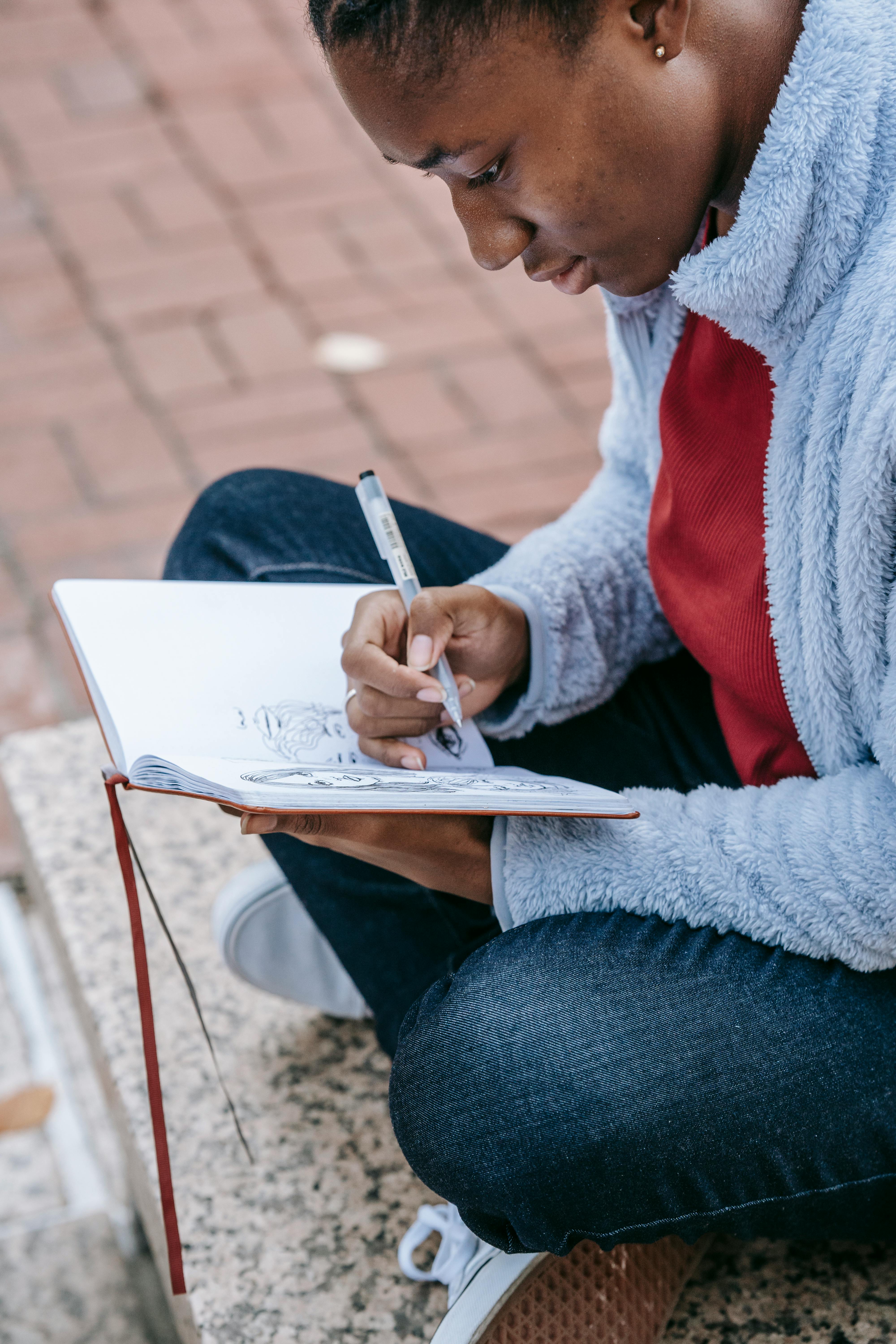 From above side view of crop focused ethnic female with crossed legs watching diary while studying on city staircase