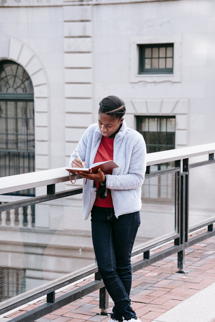 Attentive Black Student Writing In Diary On Urban Bridge