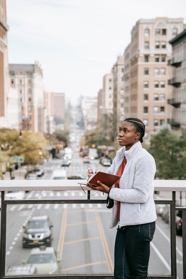 Contemplative Ethnic Student With Journal On Urban Bridge