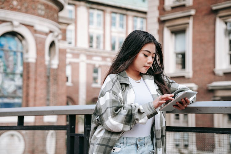 Attentive Asian Woman Chatting On Smartphone On City Bridge