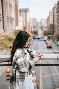 城市道路的桥上，一位千禧一代女性白天用手机上网的侧面图