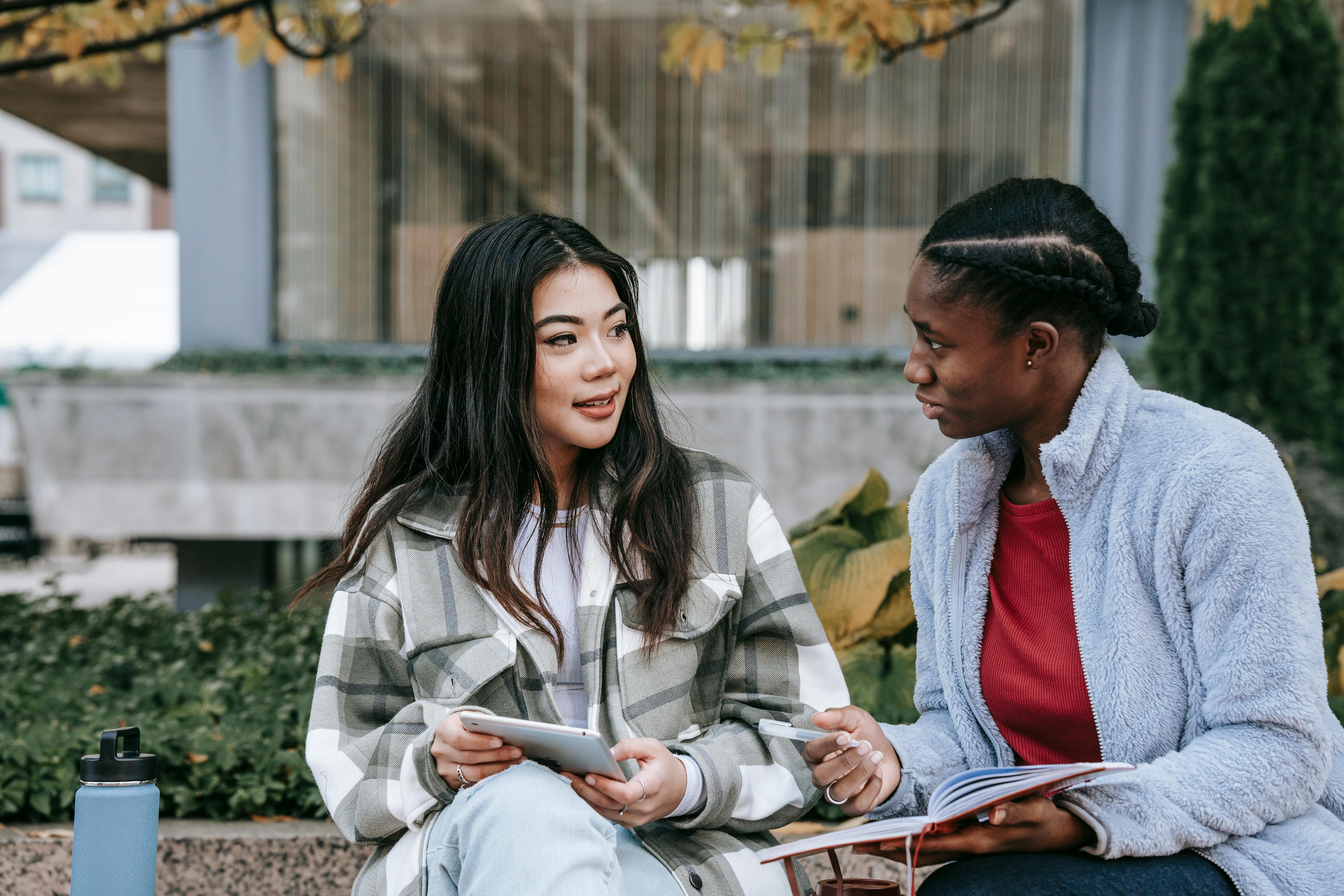 attentive multiethnic girlfriends talking while studying on urban bench